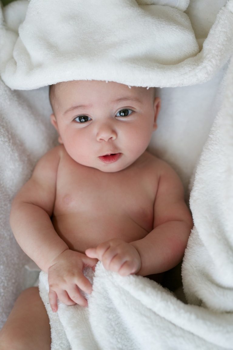 A light skinned naked baby wrapped up in a white blanket.